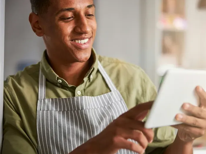 Shop owner in an apron using a tablet to manage listings, City Service Guide helps small businesses win customers